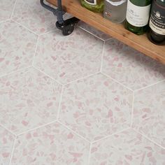 several bottles of wine on a wooden shelf in a bathroom with pink and white floor tiles