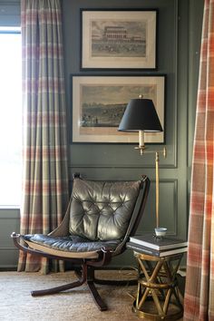 a chair and lamp in a room with pictures on the wall behind it, along with curtains