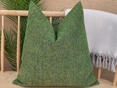 a green pillow sitting on top of a wooden bench next to a plant and white throw pillow