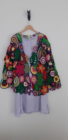 a colorful jacket hanging on a hanger next to a white wall with an object in the background