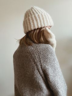 a woman wearing a white knitted hat and sweater looking off into the distance with her back to the camera