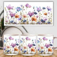 three coffee mugs sitting on top of a wooden table next to a vase with flowers