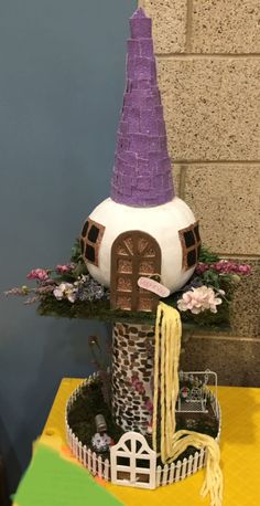 there is a cake that looks like a house with a purple hat on it's head