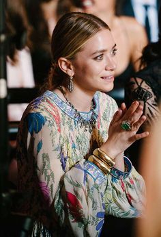 a woman standing in front of a crowd with her hands together and looking at the camera