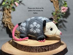 a crocheted rat is on top of a piece of wood with flowers in the background