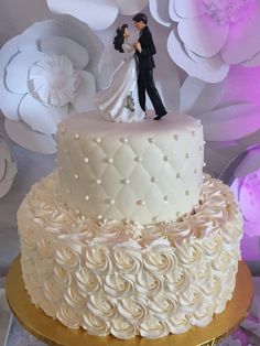 a wedding cake with a bride and groom figurine on top, surrounded by paper flowers