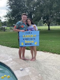 a man and woman standing next to a pool holding a sign