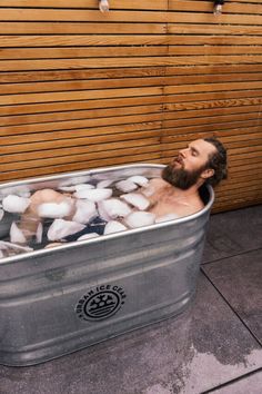 a man sitting in a tub full of ice cubes on the ground next to a wooden wall