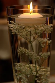 a candle that is inside of a glass vase with some flowers in it and water on the table