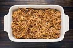 a casserole dish filled with shredded meat on top of a wooden table next to a fork