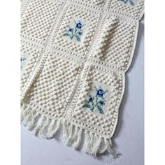 a white crocheted blanket with blue flowers on the side and fringes around it