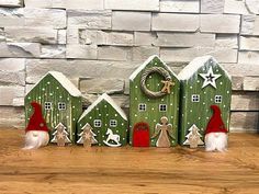 three small wooden houses with santa hats and decorations on top of a wood table next to a brick wall