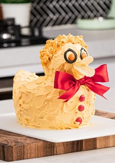 a cake shaped like a chicken with a red bow on it's head sitting on a cutting board