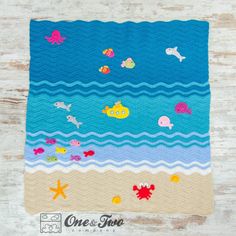 a crocheted blanket with sea animals and fish on the ocean floor next to a wooden table