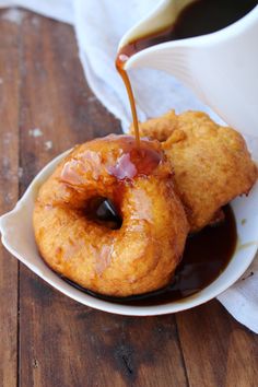 two doughnuts on a plate with syrup being poured over them and sitting on a wooden table