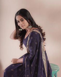 a beautiful woman in a purple dress sitting on a stool and posing for the camera