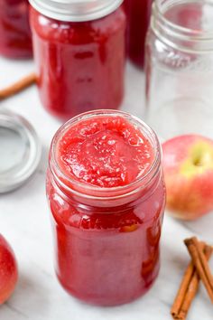 jars filled with red liquid next to cinnamon sticks and apples