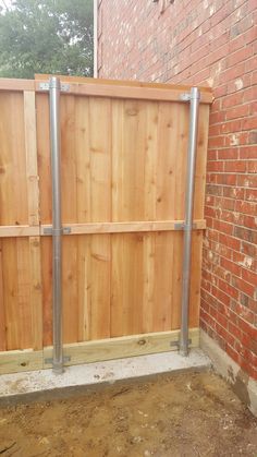 a wooden fence with metal posts in front of a brick wall