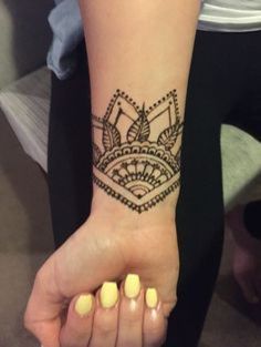 a woman's hand with a henna tattoo on her left wrist and yellow nail polish