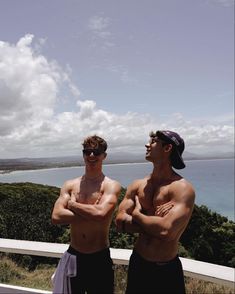 two men standing next to each other on top of a hill near the ocean with their arms crossed