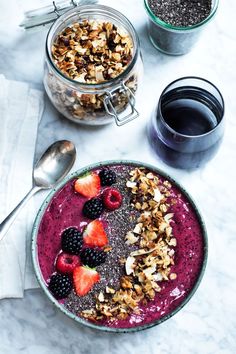 a bowl filled with fruit and granola next to two cups of coffee