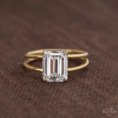 an emerald - cut diamond ring sits on a brown surface