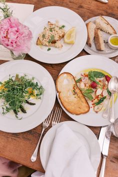 plates and silverware on a wooden table with flowers in vases next to them