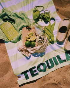 a towel that has some lemons and limes on it next to sandals, a bottle of tequila