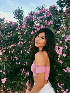 a woman standing in front of pink flowers with long hair and wearing a white dress