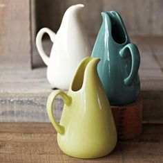 three different colored vases sitting on top of a wooden table next to each other