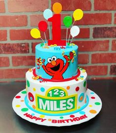 a birthday cake with the number one on it and balloons in the shape of an elmo