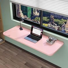 a laptop computer sitting on top of a pink desk in front of a large window