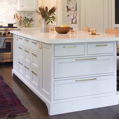 a kitchen island with white cabinets and gold pulls on the drawers, in front of an oven