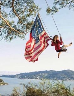 a girl is swinging on a rope with an american flag hanging from it's side