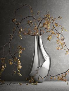 a silver vase sitting on top of a table next to a branch with flowers in it