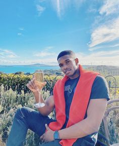 a man sitting on a bench holding a glass of wine and looking at the camera