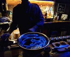 a man standing in front of a metal pan filled with blue liquid on top of a counter