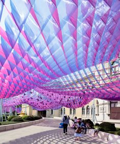 people are walking under an art installation with pink and blue ribbons hanging from the ceiling