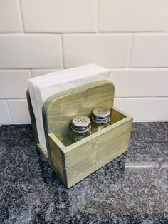 two salt and pepper shakers in a wooden box on a granite countertop next to a white tiled wall