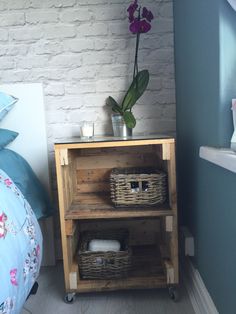 a wooden shelf with baskets on it next to a bed and a flower in a vase