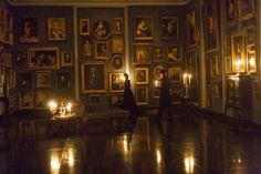 two people standing in an ornate room with candles lit up on the floor and paintings on the wall