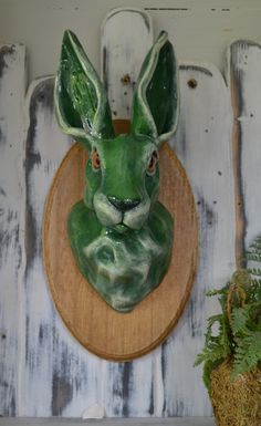 a green ceramic rabbit head mounted to the side of a white painted wood paneled wall