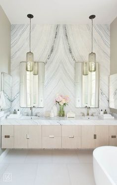 a marble bathroom with two sinks and three mirrors on the wall, along with vases filled with flowers