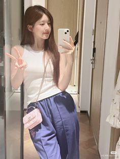 a woman taking a selfie in front of a mirror wearing blue pants and a white tank top