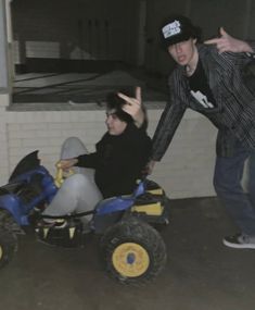 two people riding on four wheelers in an indoor garage with one person giving the peace sign