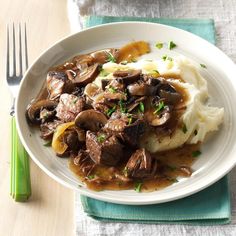 a white plate topped with mashed potatoes covered in mushrooms and gravy next to a fork