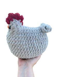 a hand holding up a knitted chicken ornament in front of a white background