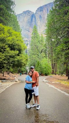 a man and woman standing in the middle of a road with mountains in the background