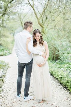 a pregnant woman standing next to her husband on a path