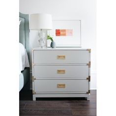 a white dresser with two drawers and a lamp next to it on top of a hard wood floor